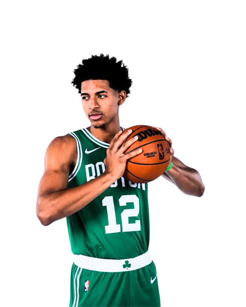 A medium shot of RJ Luis Jr. during a photoshoot. He is wearing the green Boston Celtics uniform with "BOSTON" and number 12, holding a Wilson basketball with both hands.